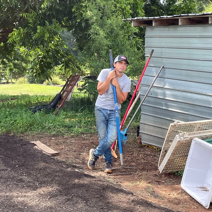 Mikey Floyd, founder of Mana Softworks, leaning on a rake at the farm